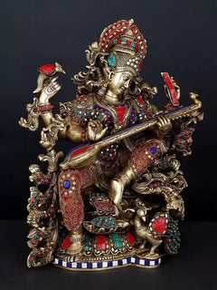 Saraswati brass statue with four arms strumming veena, red-blue gemstone-style ornaments