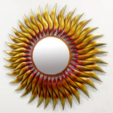 Round wall mirror with red, yellow, and gold sun-ray metal border and central glass.