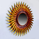 Sunburst wall mirror with a dark round center and spiked metal rays in warm tones.
