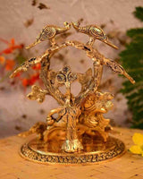 Gold-tone Radha Krishna idol under tree canopy with sculpted birds and decorative base