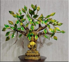 Gold metal Buddha on pedestal under leafy bodhi tree sculpture