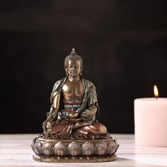 Lord Buddha resin figurine on base, gold face and folded hands beside a lit candle