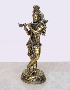 Brass Lord Krishna idol, three-quarter view with flute, detailed draped attire and base.