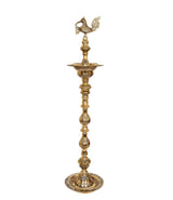 Gold-toned brass diya stand with peacock top, stacked tiers and ornate round foot
