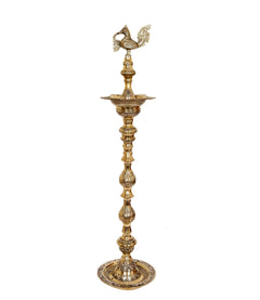 Gold-toned brass diya stand with peacock top, stacked tiers and ornate round foot