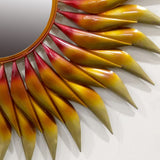 Close-up of pointed metal sun rays in gold and red tones along the mirror edge.