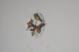 Gold-tone iron bird wall decor on branch with circular white backplate, angled view