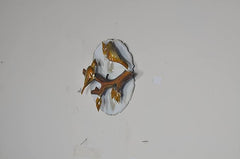 Gold-tone iron bird wall decor on branch with circular white backplate, angled view