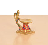 Side view of brass peacock diya oil lamp, red skirt with blue and gold detailing