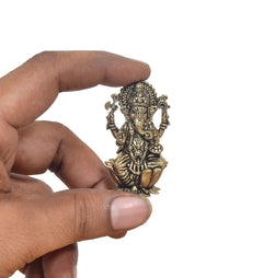 Hand holding a small bronze Ganesha statue seated on a lotus base.