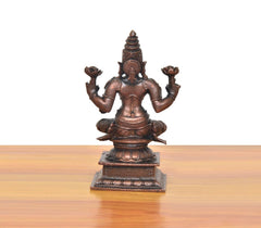 Back view of copper Lakshmi idol, seated figure with four raised arms and tall crown.