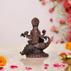 Copper Saraswati figurine back view, seated on ornate base with tail-like decoration