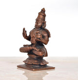 Copper Dhanvantari statue side view, seated with one hand raised, stepped base