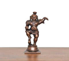 Copper Bal Krishna showpiece, dancing stance holding laddu, front view on round base