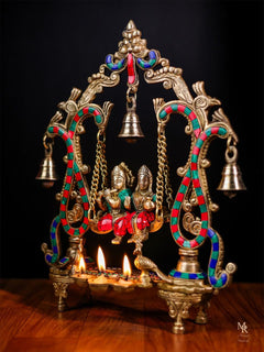 Radha Krishna swing idol with bells and diya tray, colorful beaded detailing, lit lamps