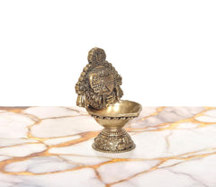 Brass oil lamp figurine with engraved deity panel and ornate base, side view