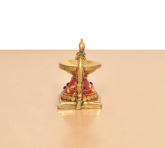 Brass peacock diya oil lamp from back, red-and-gold body with multicolor accents