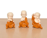 Three small seated monk Buddha resin sculptures, orange robes and bald heads