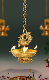 Brass hanging peacock diya oil lamp with chain, ornate bird top, and lit flames