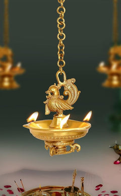 Brass hanging peacock diya oil lamp with chain, ornate bird top, and lit flames
