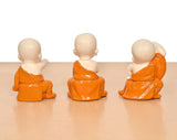 Back view of three seated monk Buddha resin sculptures in orange robes