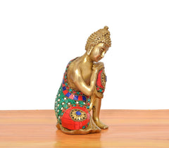 Profile view of brass seated Buddha idol, hands folded, multicolor robe