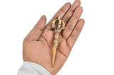 Brass furba phurpa upright in palm, dorje vajra crown detail at the handle