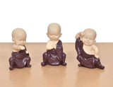 Set of three purple resin monk Buddha figurines, seated poses, straight-on view