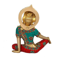 Side view of brass Indra Devta statue, seated, teal top with red jeweled leg wrap.