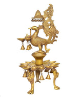 Golden peacock-shaped diya stand with hanging bells, brass oil lamp showpiece.