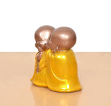 Resin laughing Buddha sculpture, side view of two monk figures in glossy yellow robes