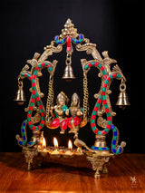 Radha Krishna swing idol with hanging bells, colorful beaded arches, diya lamps lit