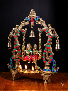 Radha Krishna swing idol with hanging bells, colorful beaded arches, diya lamps lit