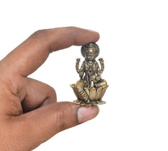 Hand holding a small bronze Lakshmi statue seated on a lotus base.