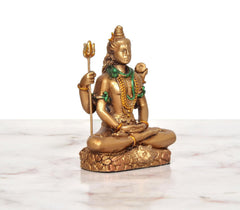 Seated Shiva idol with four arms, gold resin, green accents, holding trident