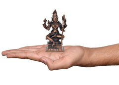 Rajarajeshvari statue on open palm, seated four-armed deity, copper tone, 4.5 in.