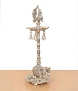 Silver metal peacock diya stand with hanging bell-like cups and elephant base