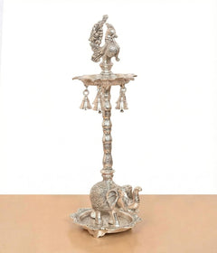 Silver metal peacock diya stand with hanging bell-like cups and elephant base