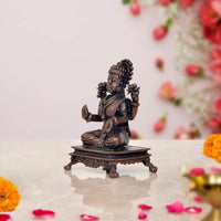 Side view of Lakshmi seated on pedestal, raised hands and detailed jewelry