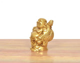 Seitenansicht: Lachender Buddha in goldfarbigem Messing, sitzendes/stehendes Gewanddetail