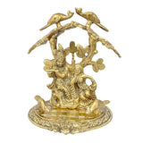 Gold-tone Radha Krishna idol under tree with birds, front view on textured base