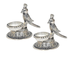 Two parrot-shaped oil diya lamps with long wings and detailed swirling engravings