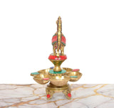Back view of brass oil lamp on five-diya tray, peacock finial and painted accents