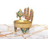 Brass diya lamp on three feet, teal-and-gold naama emblem, chakra design behind