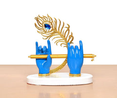Krishna Deko auf weißem Sockel: blaue Hände mit goldener Flöte, goldener Federkranz