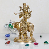 Brass Krishna statue on cow, Krishna holding flute, ornate gold-tone details