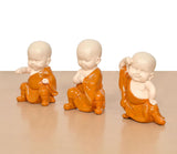 Seated monk Buddha resin sculptures from the side, orange robes