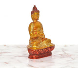 Brass Buddha idol seated, Abhaya mudra hand position, golden robe, red-gold lotus base