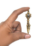 Hand holding small brass dorje vajra furba with decorative crown-like top