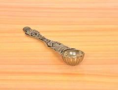 Bronze pooja spoon with central scroll detailing and textured, ribbed bowl edge